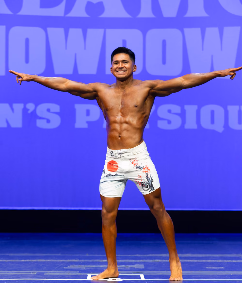 Mark Villanueva Jr. on stage at a men's physique competition